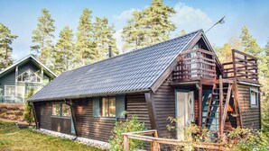 Une cabane rustique en rondins de bois, avec un toit en métal, une terrasse en bois et une échelle menant à une mezzanine.