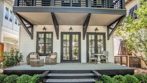 Une maison à deux étages avec un porche couvert, des marches menant à l’entrée et du mobilier d’extérieur.