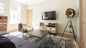 Un salon comprenant un canapé, une table basse, un téléviseur, un meuble en bois et un lampadaire.