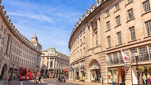 Une vue de rue avec des bâtiments historiques, un autobus à deux étages rouge et des devantures de magasins, dont une affiche bien visible de « Uni Qlo ».