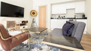 Un salon moderne comprenant un canapé, une table basse, un téléviseur à écran plat et un coin cuisine avec des placards et des appareils électroménagers.