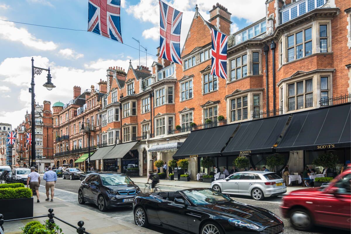Una hilera de edificios de ladrillo rojo con varias banderas, incluyendo la Union Jack, y escaparates con letreros como "Scott's".