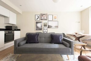 A modern living room with a grey sofa, a dining table, and a kitchen area with white cabinets and a black countertop. - The New Bond Street Loft - Modern 1bdr City Centre Apartment (London)