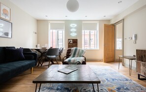 A modern living room with a dark sofa, a coffee table, and a dining area with chairs and a table. - The New Bond Street Loft - Modern 1bdr City Centre Apartment (London)