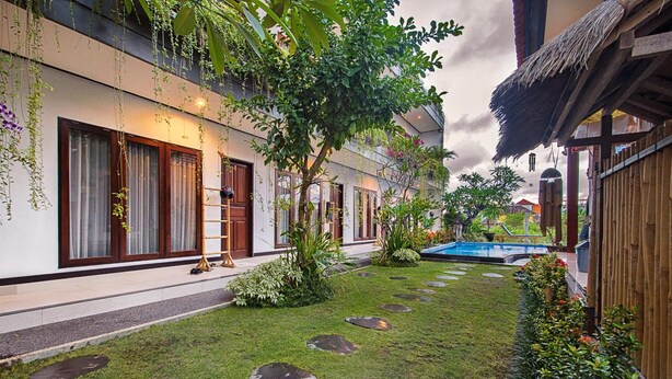 Un patio con piscina, piedras de adoquín y abundante vegetación.