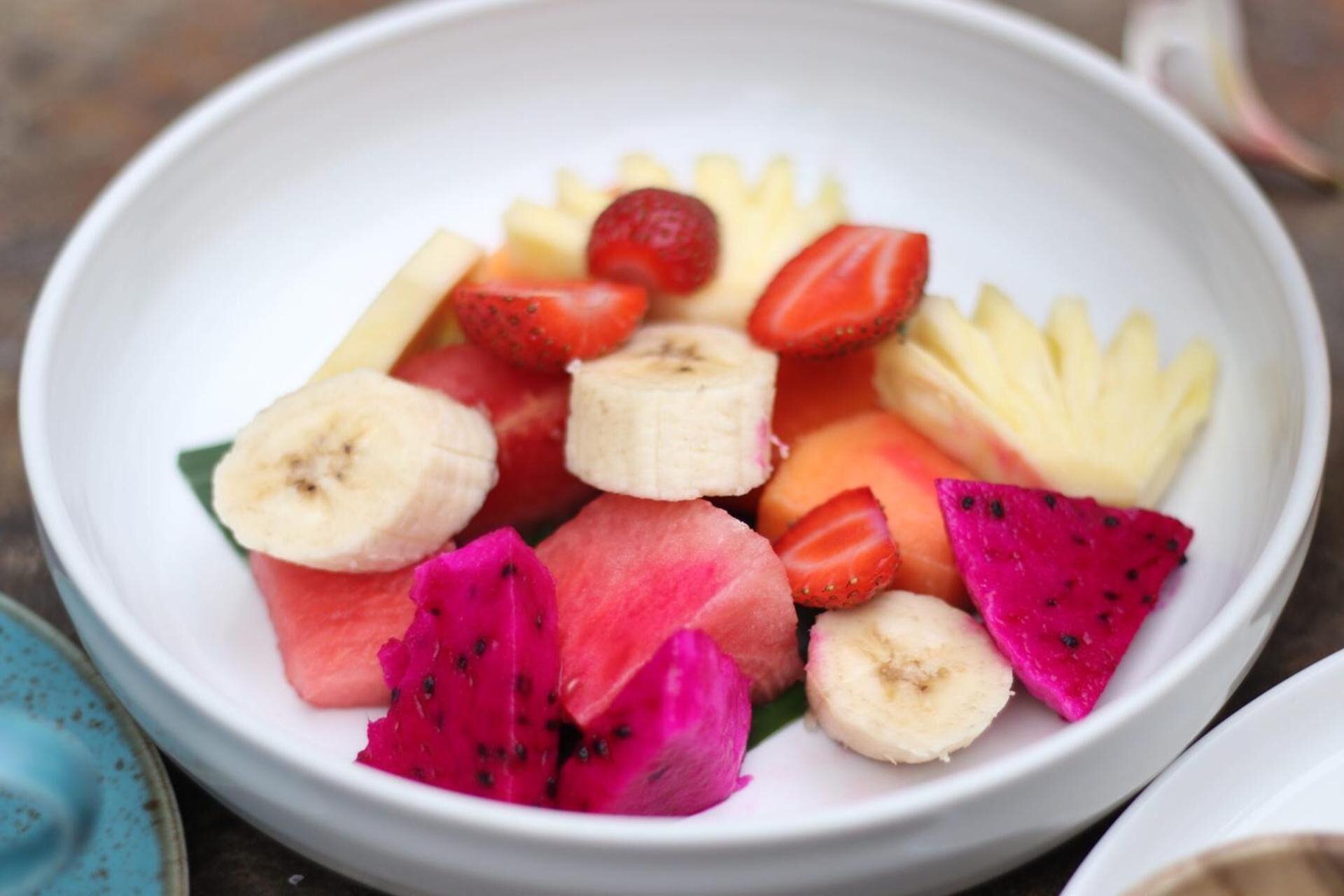 A bowl of assorted fruits including bananas, strawberries, watermelon, and dragon fruit.