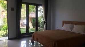 Un dormitorio con una cama grande, una puerta corrediza de vidrio que da a un jardín y vistas al exterior.