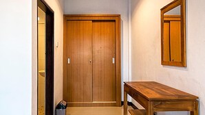 Un pasillo con puerta de madera, un espejo, una mesa de madera y un cesto de basura.