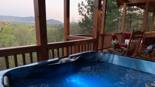 Tinaco de hidromasaje en una terraza de madera, con vista a un bosque y montañas.