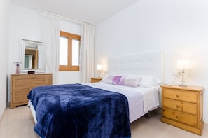 A bedroom with a bed, a wooden dresser, a nightstand, a mirror, and a window with curtains.