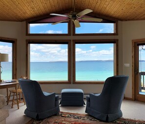 A room with a large window overlooking a body of water, a ceiling fan, and two blue chairs.
