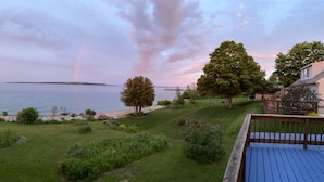 A view of a lakeside property with a deck overlooking the water, surrounded by greenery and a distant island. - Huron Haven in St. Ignace (Saint Ignace)