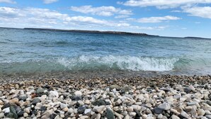 A pebbled beach with clear water and a distant shoreline. - Huron Haven in St. Ignace (Saint Ignace)