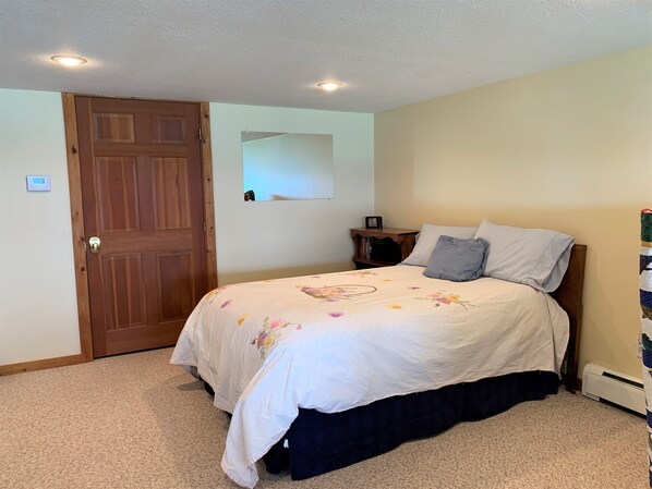 A bedroom with a wooden door, a bed with floral bedding, a nightstand, and a mirror on the wall.