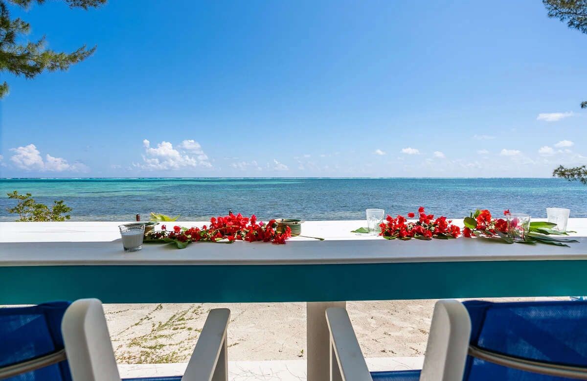 A view from a balcony overlooking a beach with a table set with flowers and glasses.