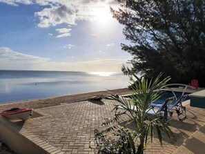 A poolside area with a view of the sea, a lounge chair, and a red chair. - The peace and tranquility of this cottage Works Wonders on the soul.... (Grand Cayman)