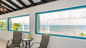 Ein Zimmer mit zwei Stühlen und einem kleinen Tisch, große Fenster mit Meerblick und einer Decke mit freiliegenden Balken.