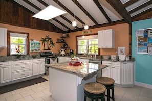 Et køkken med lyse skabe, en køkkenø med barstole og et skilt der står 'Happy Hour'.