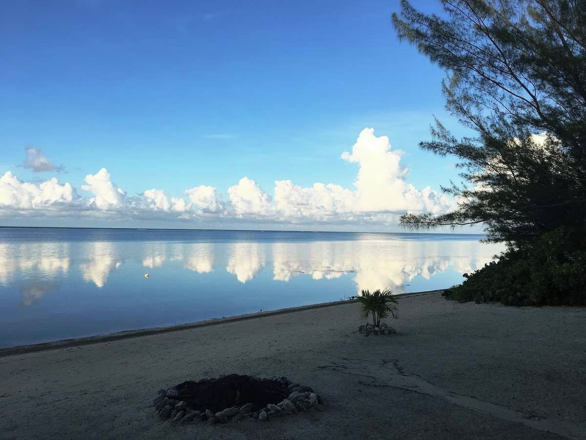A beach with calm water, a clear sky, and a small fire pit.