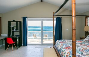 Een slaapkamer met een bed, bureau, stoel en uitzicht op zee vanaf een balkon.