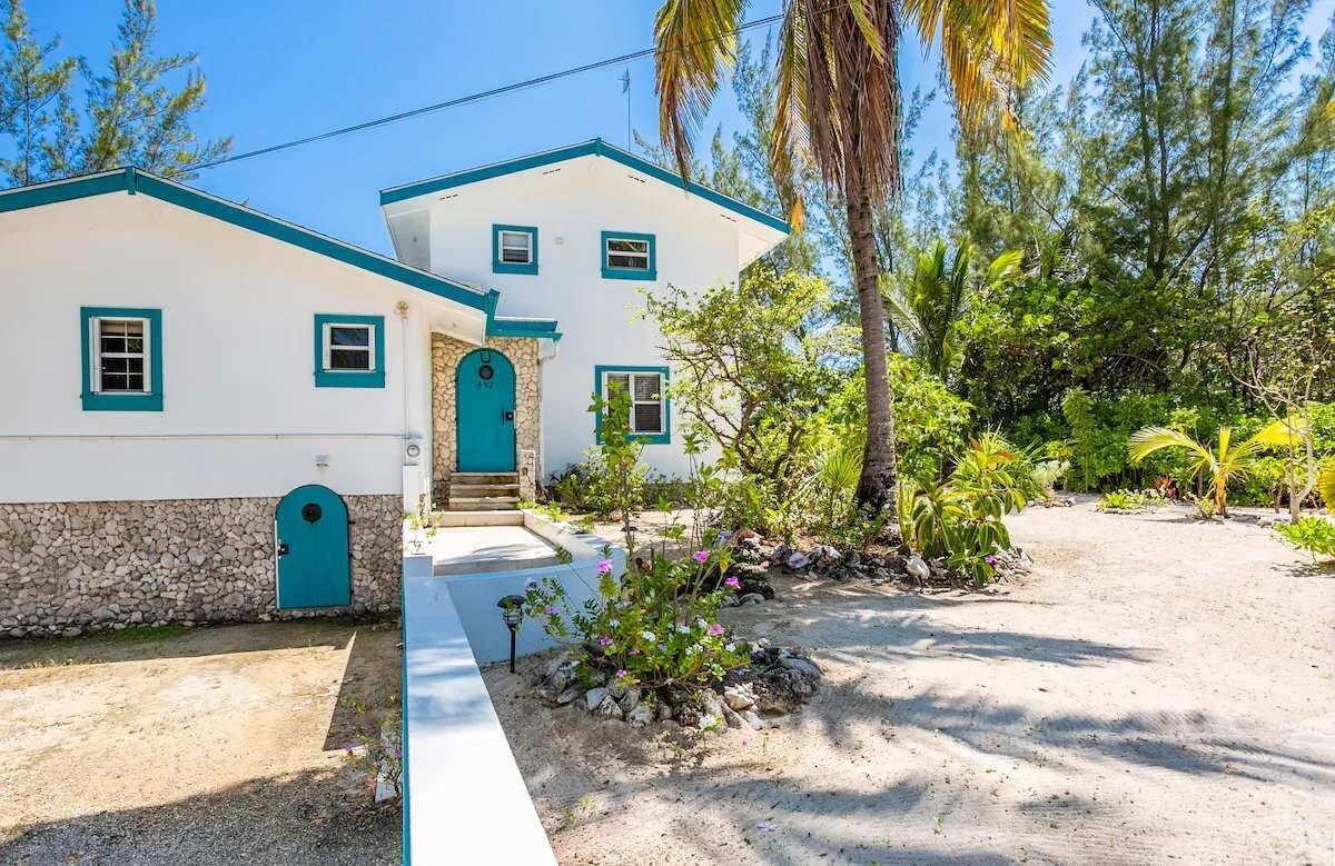 A two-story house with a stone foundation, a blue door, and a small porch with plants.