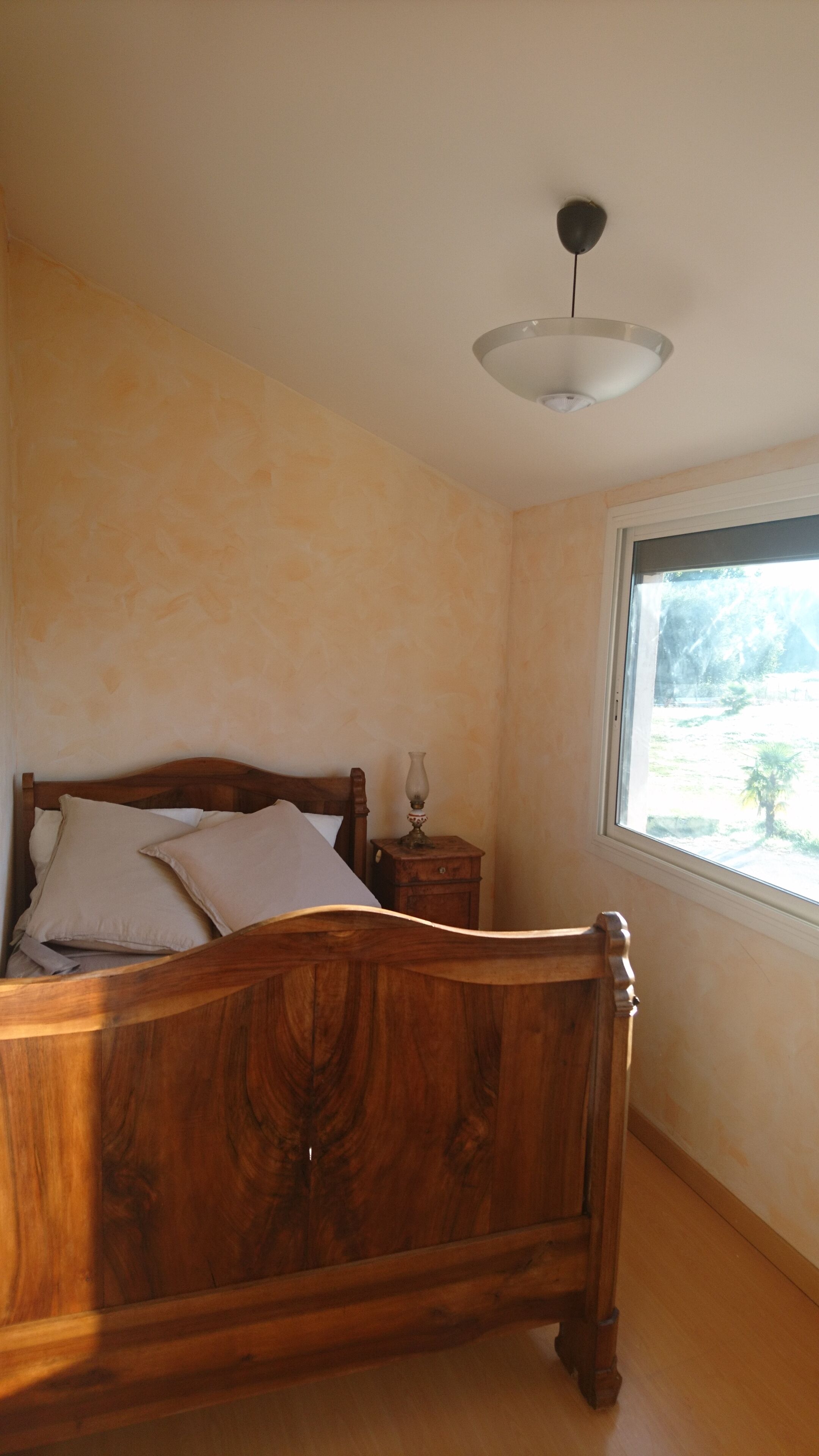 A bedroom with a skylight, a wooden bed, a bedside table, and a wall-mounted light fixture.