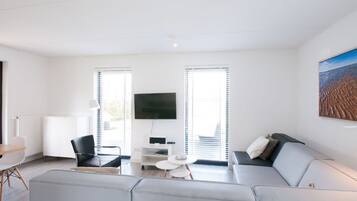 Una sala de estar moderna con un sofá gris, una mesita blanca y un televisor montado en la pared.