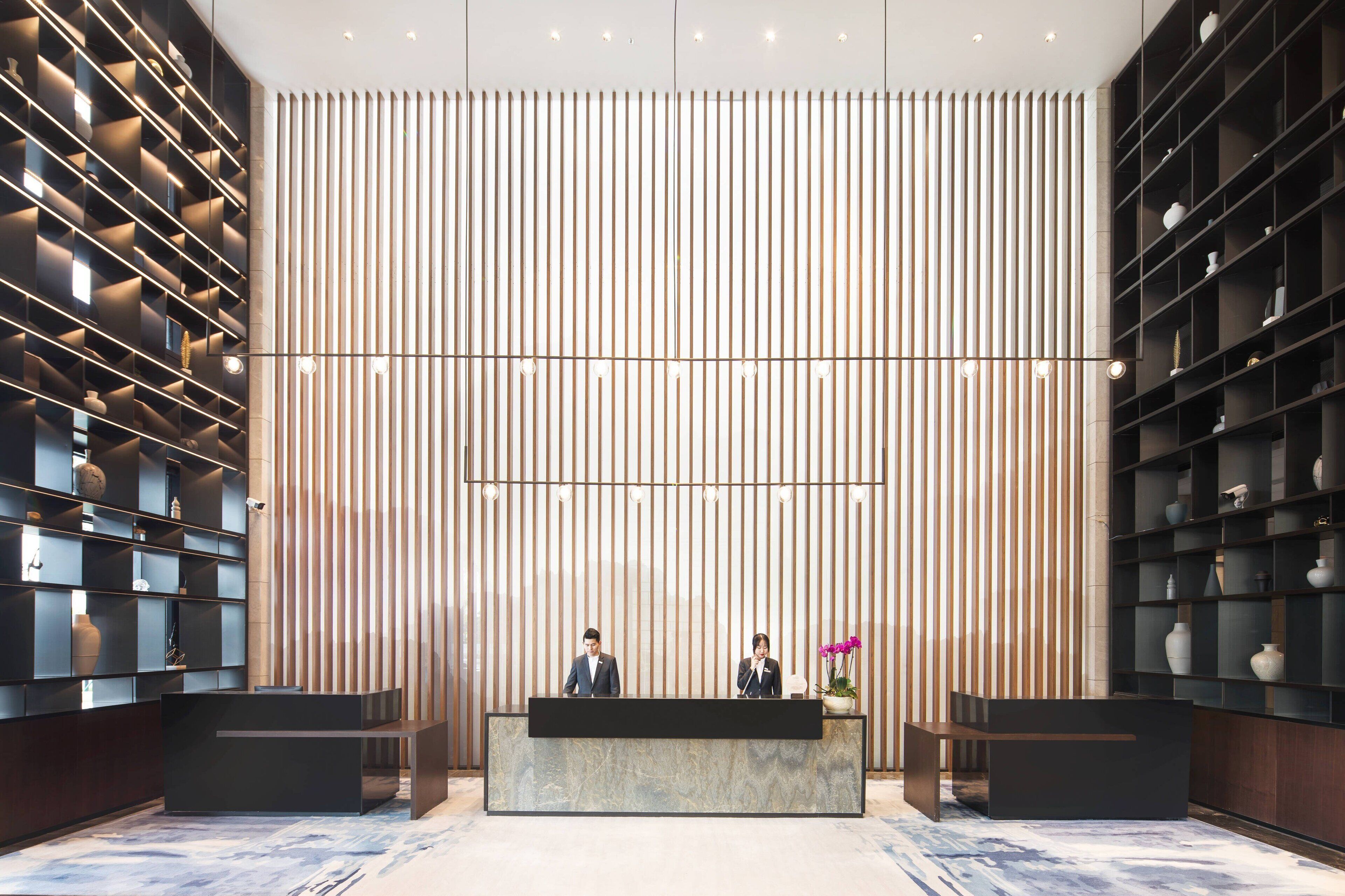 A reception desk with two staff members, flanked by shelving units with decorative items.