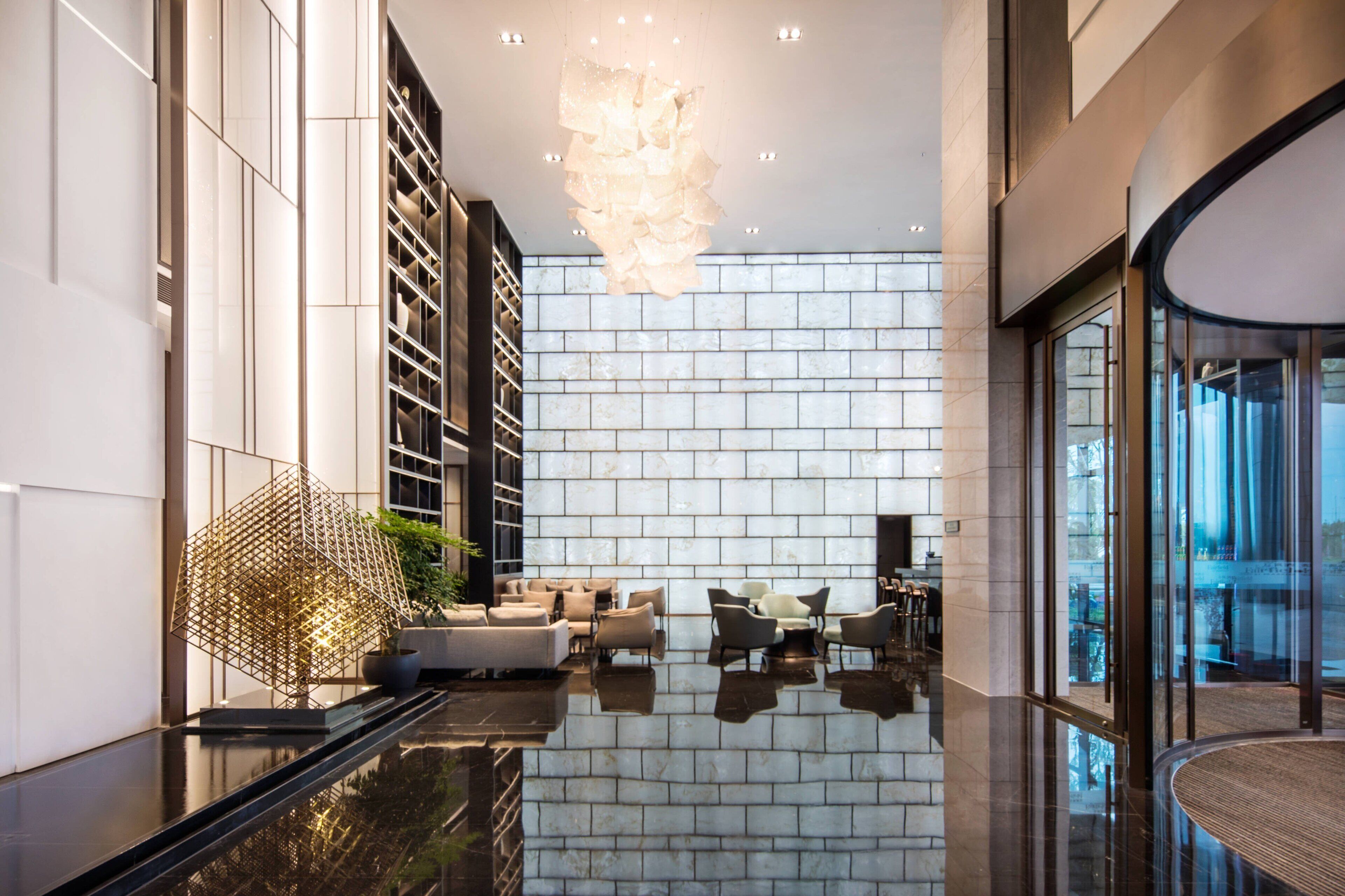 A modern lobby with a reflective floor, a geometric light fixture, and a seating area with sofas and chairs.