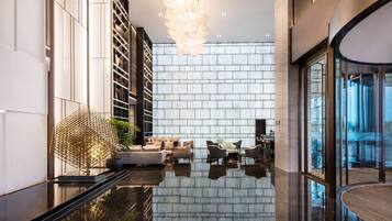 A modern lobby with a reflective floor, a geometric light fixture, and a seating area with sofas and chairs.