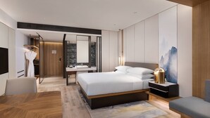 Una habitació d'hotel moderna amb un llit gran, taules de nit, un escriptori i una cadira. Hi ha un bany amb un mirall i un lavabo.