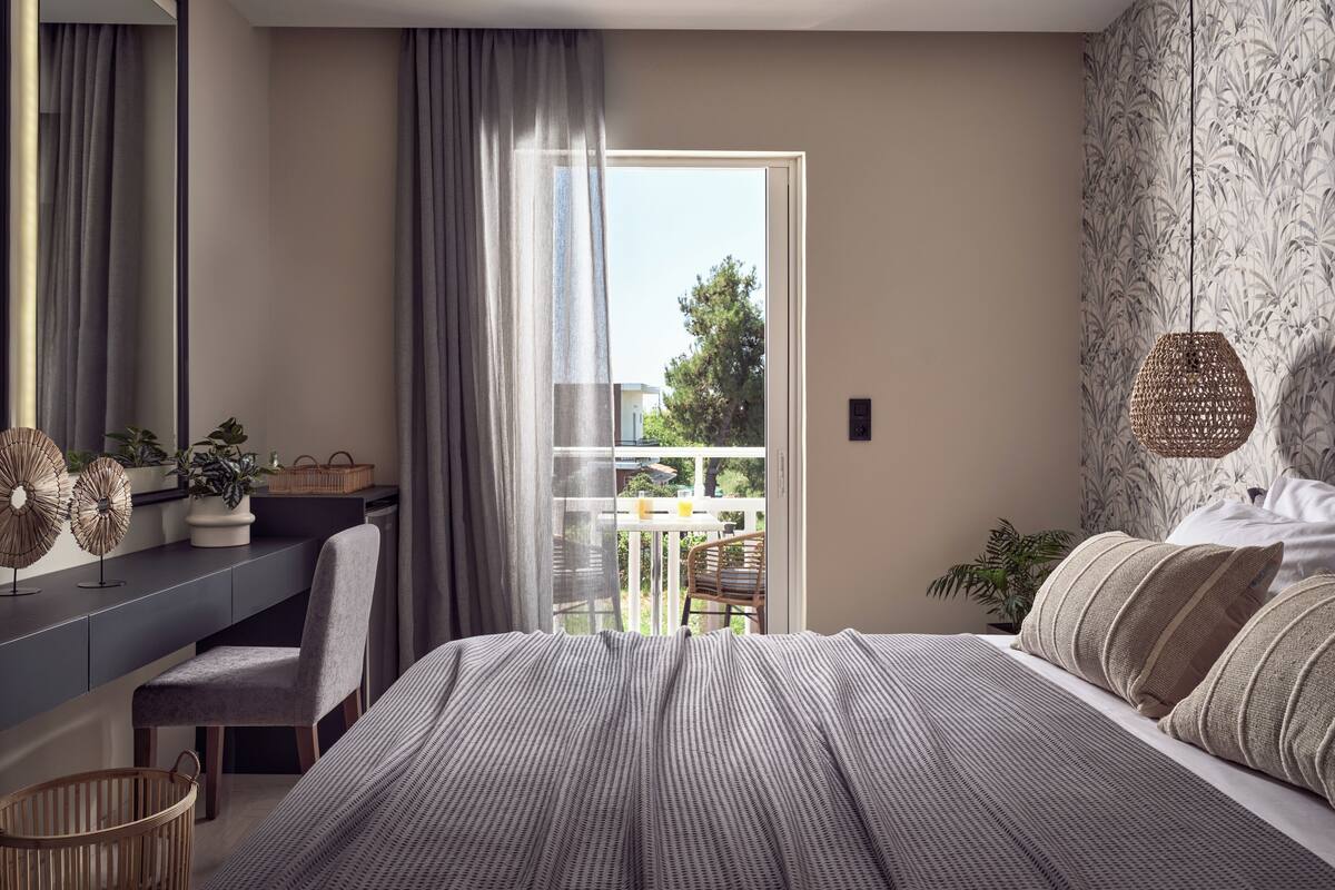 A bedroom with a bed, a desk, a chair, a window, and a balcony.