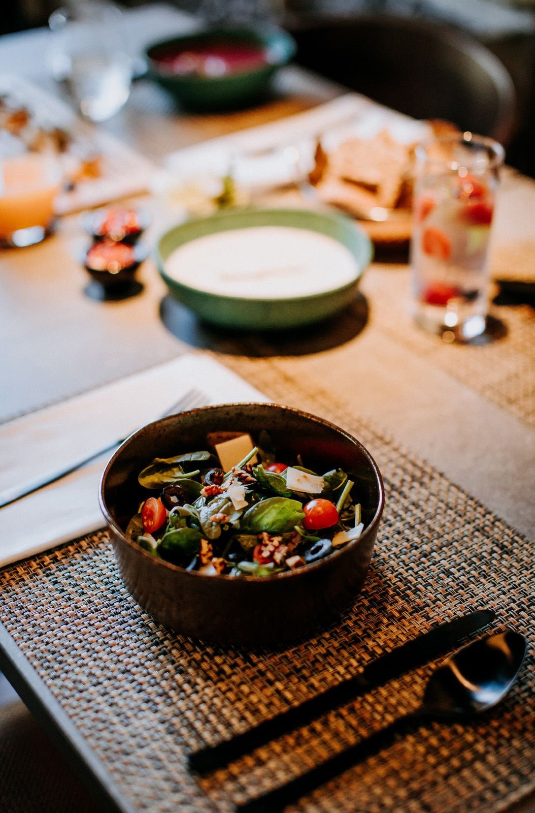 Una mesa de comedor con un tazón de ensalada, un tazón verde y un vaso de agua.