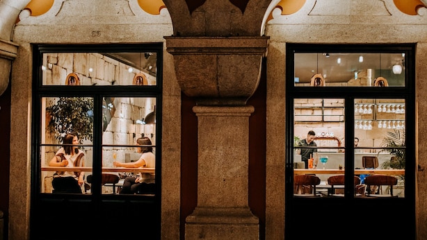 Un restaurant doté de fenêtres en arc de cercle et de colonnes en pierre, avec un intérieur aux murs en briques et un bar visible à travers les fenêtres.