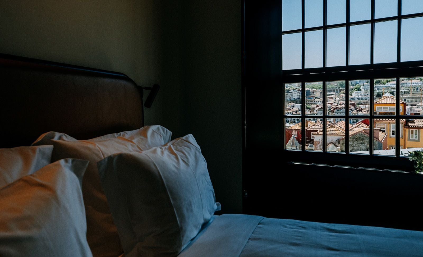 A bed with white linens and a view of a cityscape through a window with a grid pattern.