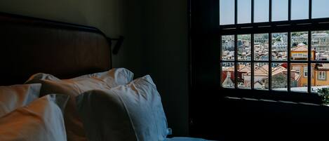 A bed with white linens and a view of a cityscape through a window with a grid pattern.
