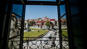 Une vue depuis une fenêtre donnant sur un paysage urbain, avec des bâtiments, une statue et un espace vert traversé par un passage piéton.
