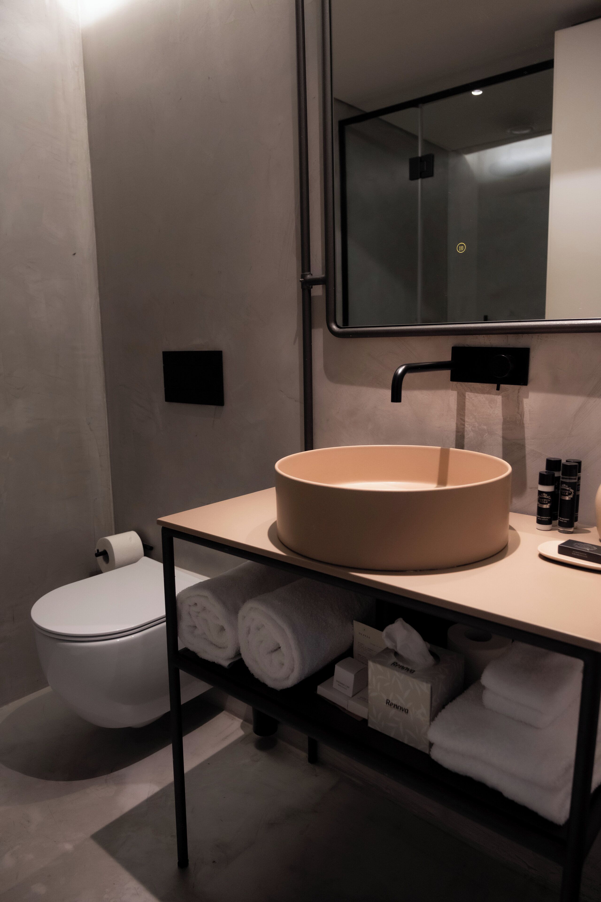 Une salle de bain moderne avec un lavabo rond, des toilettes et un porte-serviettes sur lequel sont pliées des serviettes.