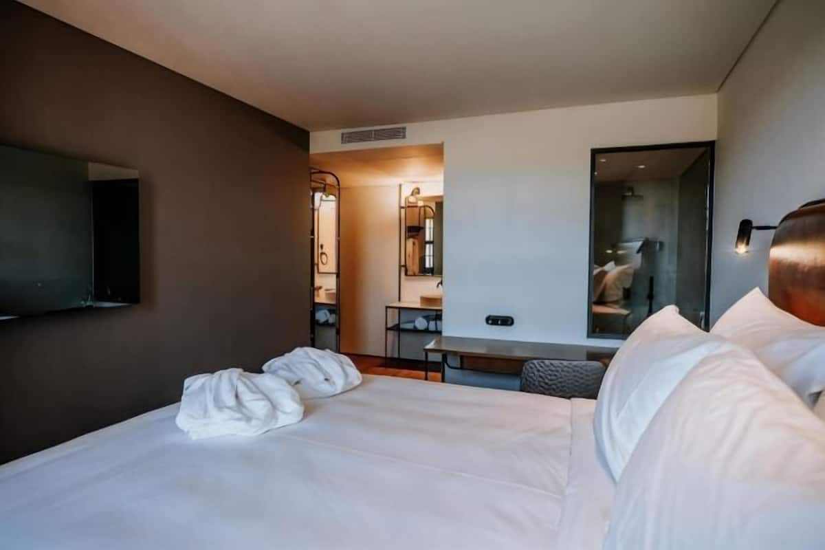 A hotel room with a bed, a desk, a mirror, and a TV.