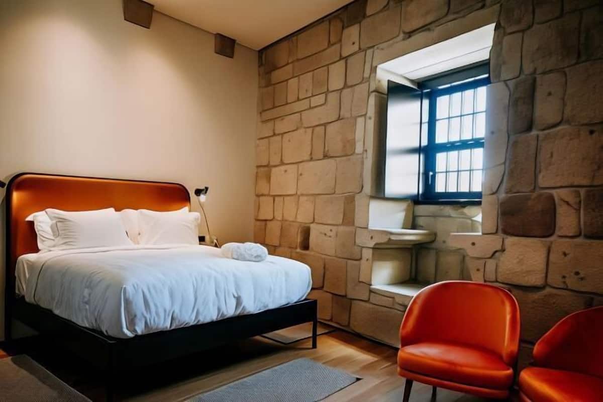 A bedroom with a stone wall, a bed, a window, and a red chair.