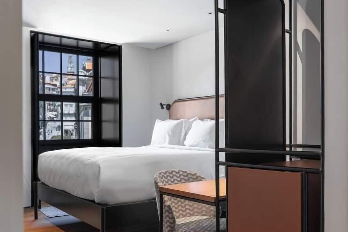 A modern hotel room with a bed, a desk, and a view through a window.