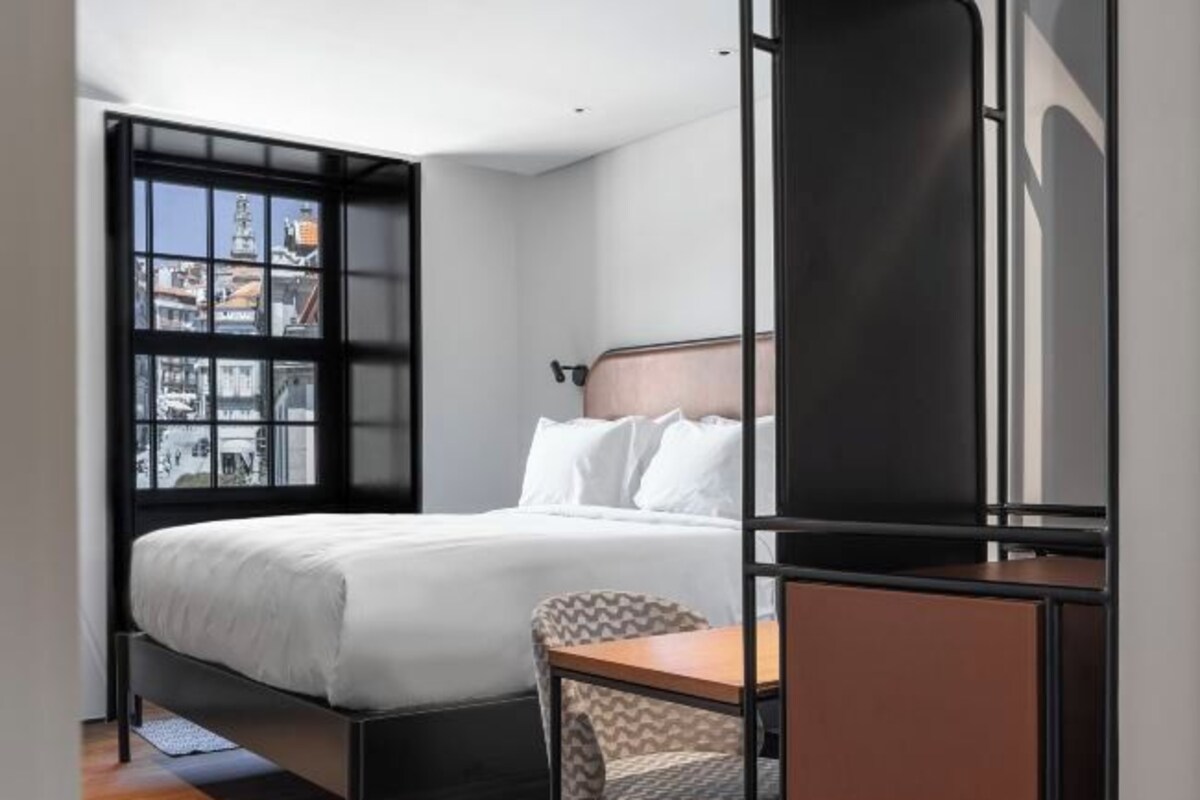 A modern hotel room with a bed, a desk, and a view through a window.