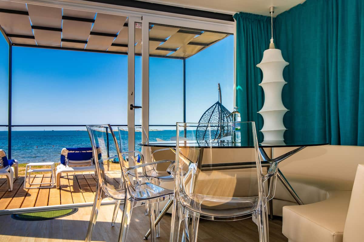 A deck with clear chairs and a table, a white lamp, and a view of the sea.