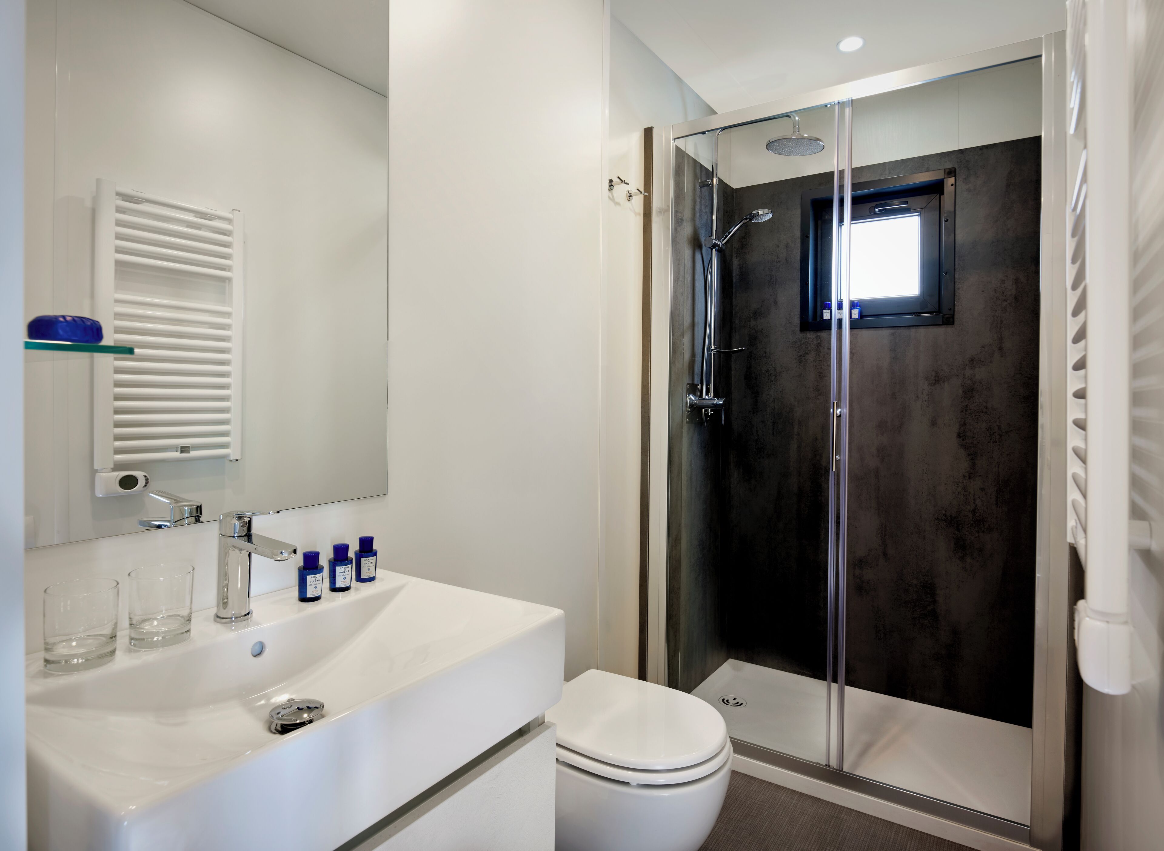 A modern bathroom with a glass-enclosed shower, a white sink with a mirror above it, and a toilet.