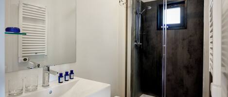 A modern bathroom with a glass-enclosed shower, a white sink with a mirror above it, and a toilet.