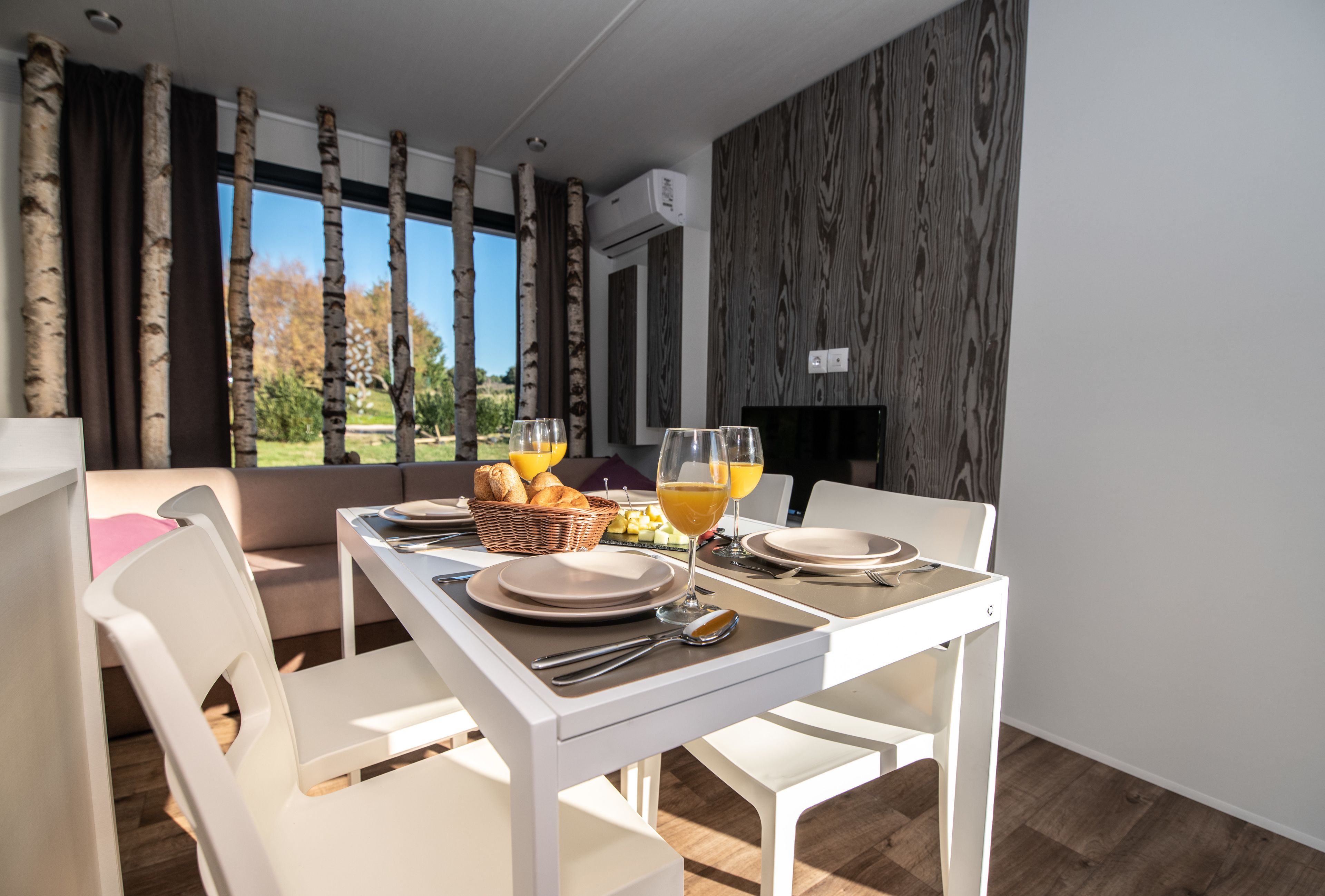 A dining area with a table set for two, including plates, cutlery, and glasses of orange juice.