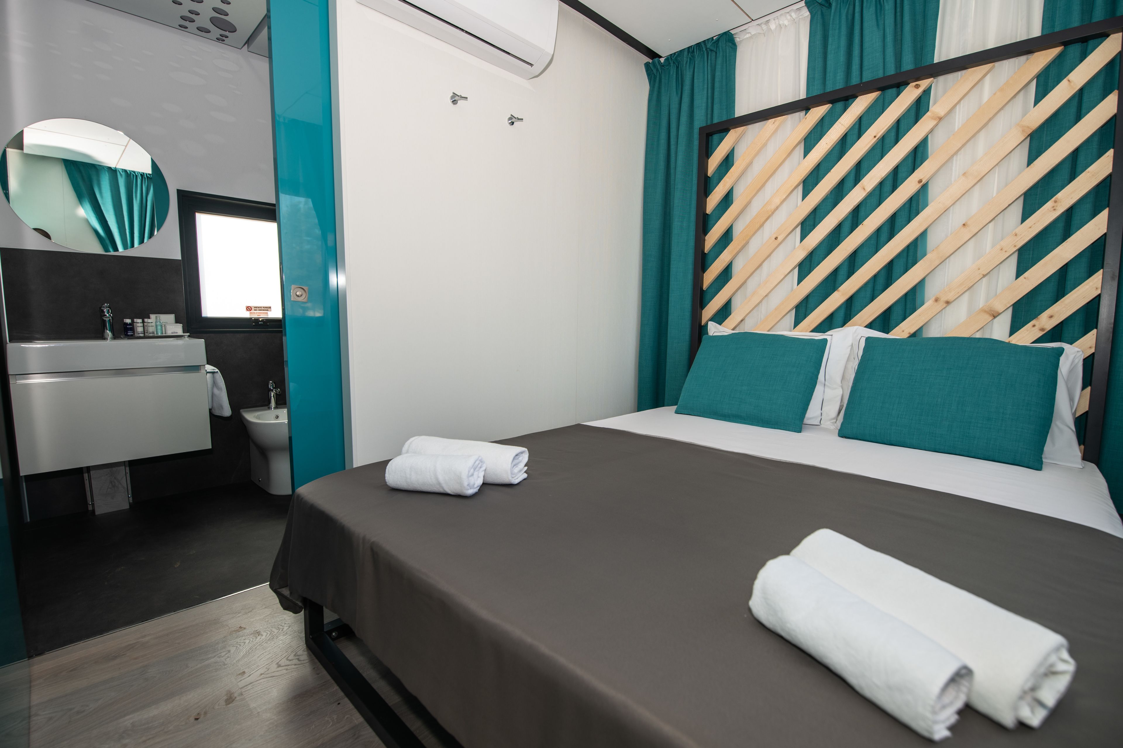 Una habitación de hotel con cama, baño con lavamanos y espejo, y cortinas color turquesa.