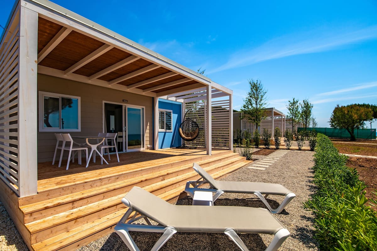 A modern cabin with a wooden deck, outdoor seating, and a swing chair.