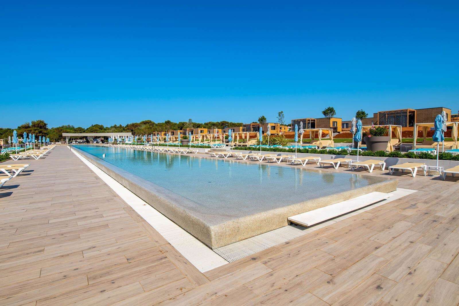 A pool area with lounge chairs and umbrellas, surrounded by buildings with a modern design.
