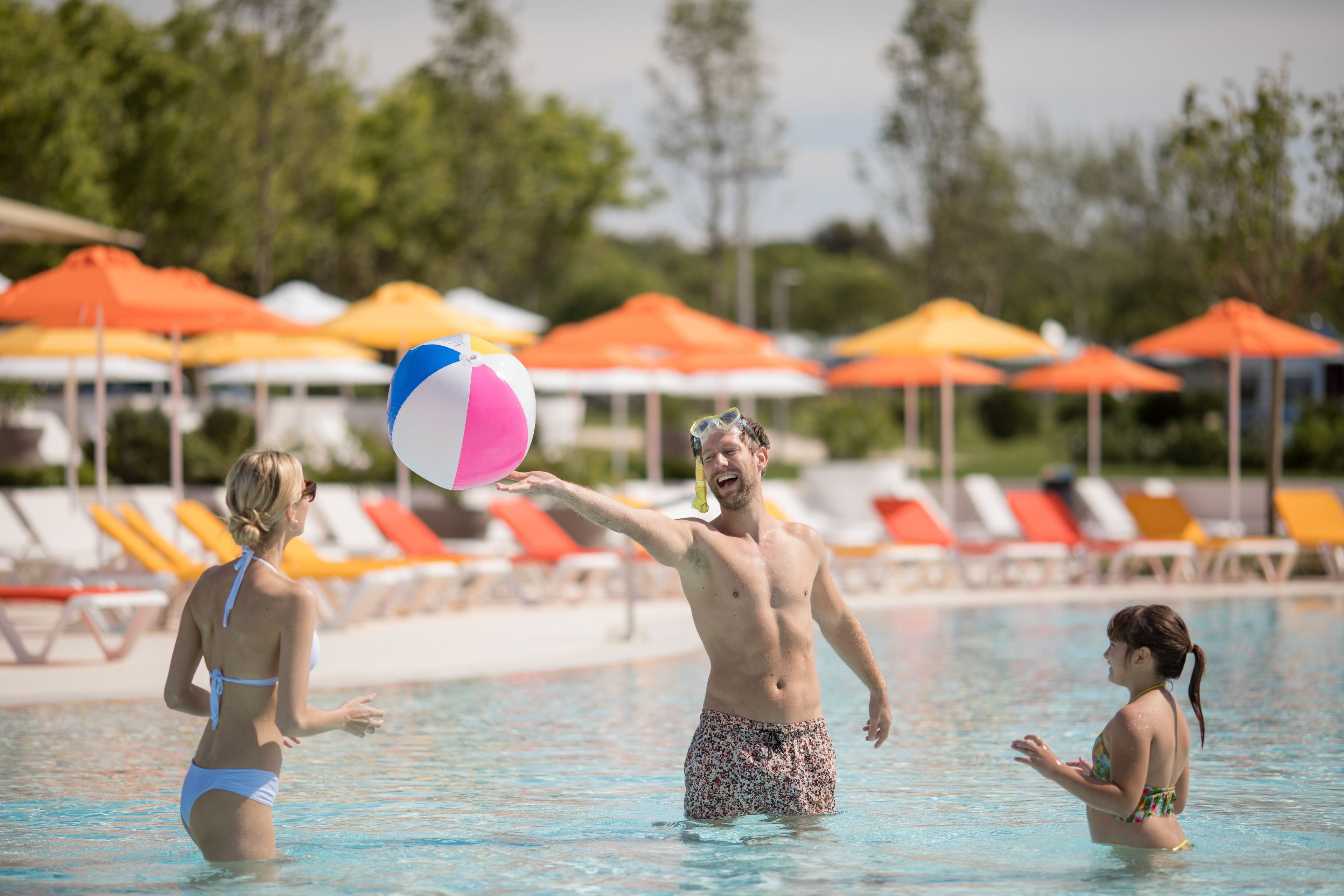 A swimming pool with people playing with a beach ball.